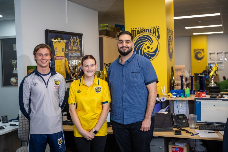 3 people standing in the Central Coast Mariners office side by side smiling