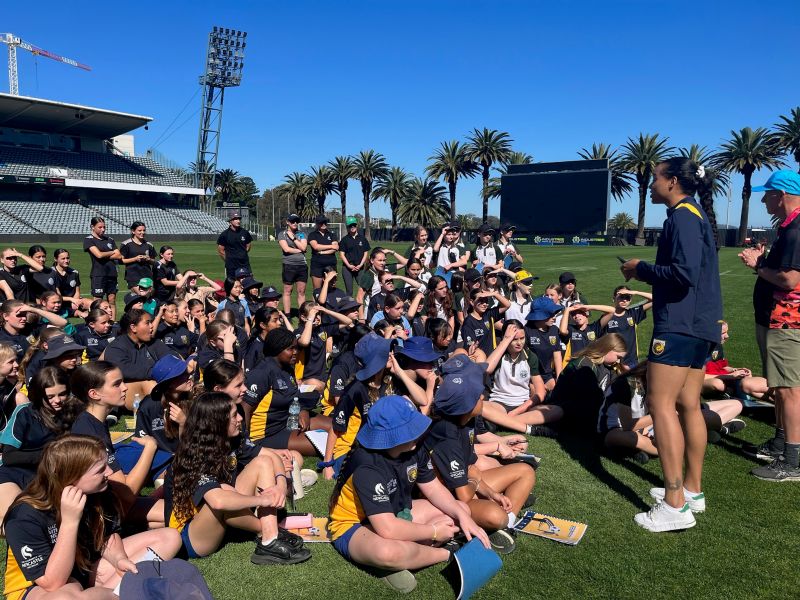 Group of School students sitting on a soccer field with a teacher standing up and speaking to them
