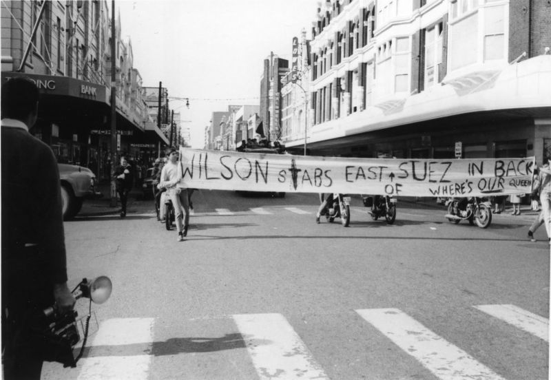 A group of people walking through the street with a sign