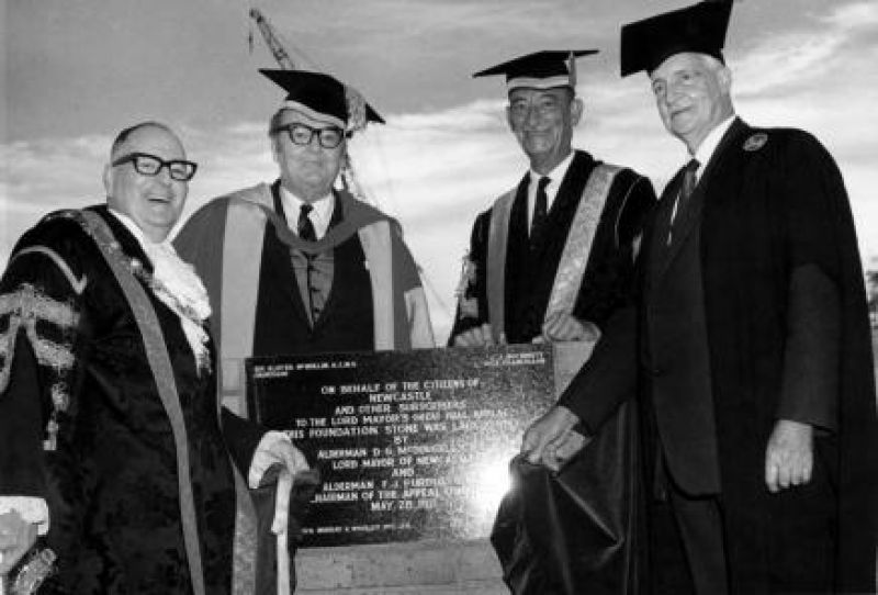 Four men standing in front a plaque