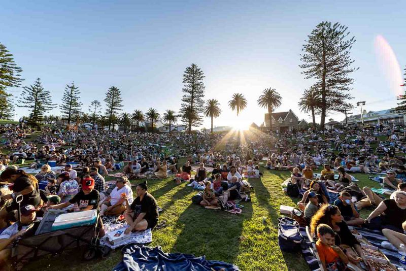 A large group of people sitting in a grassy reserve